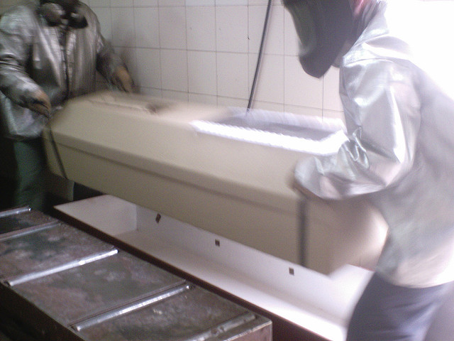 Dos trabajadores en su indumentaria, alzando un ataúd de cartón, durante su jornada