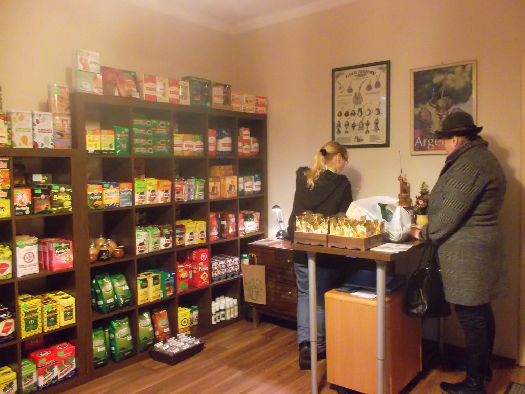 Tienda con cajas que contienen yerba mate. Una mujer mayor hace fila se prepara para pagar en el mostrador.